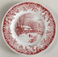 a red and white plate with a house in the snow on it, surrounded by trees