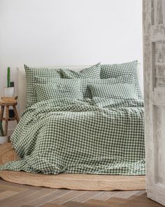 a green and white checkered comforter set on a wooden floor next to an open door