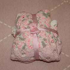 a pink and white teddy bear is laying on the floor next to a blanket that has been crocheted with flowers