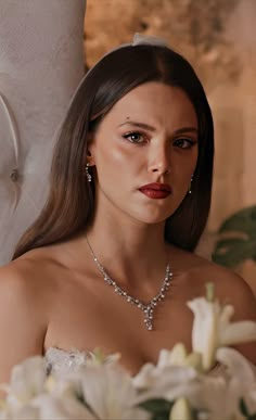 a woman in a white dress wearing a necklace and earrings with flowers around her neck