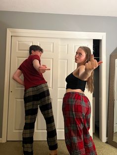 two people standing in front of a door with one pointing at the other person wearing plaid pants