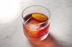 a glass filled with liquid and an orange peel on top of it next to a marble table