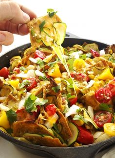 someone is dipping some tortilla into a skillet filled with vegetables and other toppings