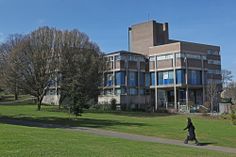 a person walking down a path in front of a building on a sunny day with trees and grass