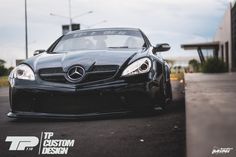 the front end of a black sports car parked in a parking lot next to a building