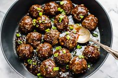 meatballs with sauce and green onions in a skillet on a marble counter top