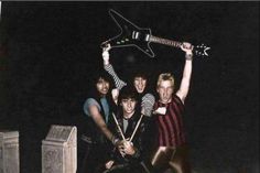 four young men are posing for a photo with an electric guitar on their shoulders and arms in the air