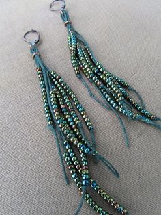 two pairs of beaded earrings hanging from hooks on a gray cloth covered tablecloth