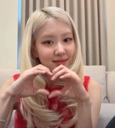 a woman sitting on top of a couch making a heart shape with her hands in front of her face