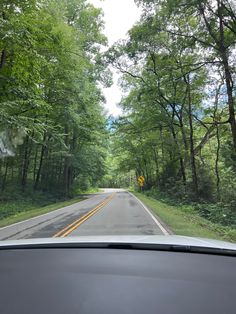 a car driving down a road next to lush green trees and tall, leafy trees