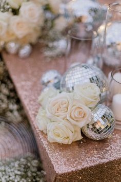 white roses and silver disco ball centerpieces on a pink table cloth with candles