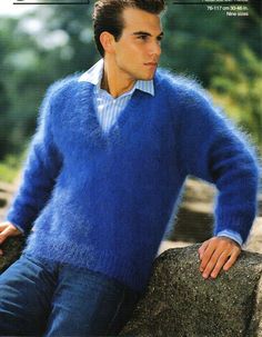 a man in a blue sweater leaning on a rock