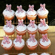 twelve cupcakes with pink bows on them sitting on a cooling rack