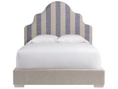 an upholstered bed with white and gray striped linens on the headboard