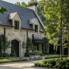 a large stone house with lots of trees and bushes around it's front entrance