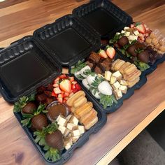 three plastic trays filled with food on top of a wooden table next to each other