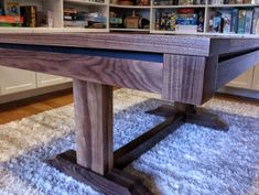 a wooden table sitting on top of a white rug in front of a book shelf