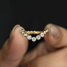 a person holding a gold ring with five diamonds on it's side and their fingers