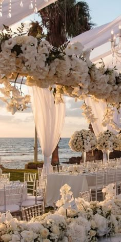 an outdoor wedding set up with white flowers and greenery on the beach at sunset