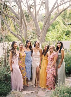 a group of women standing next to each other in front of trees and bushes on a sunny day