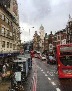 a red double decker bus driving down a street next to tall buildings and parked bicycles