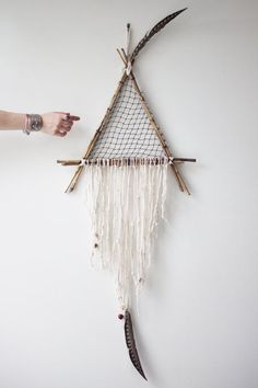 a person pointing at a wall hanging made out of bamboo sticks and yarn with the word crochet dream catcher written on it