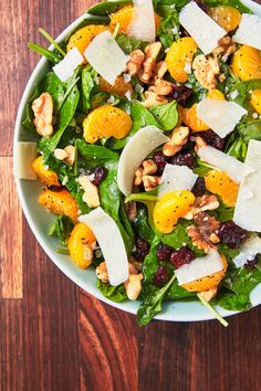 a salad with oranges, nuts and cheese in a white bowl on a wooden table