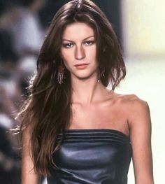 a woman with long hair walking down a runway wearing a strapless top and earrings