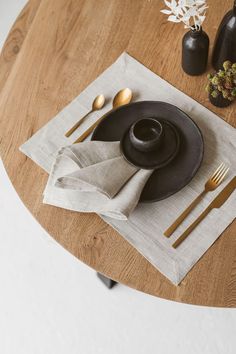 a wooden table topped with a black plate and silverware on top of a white napkin