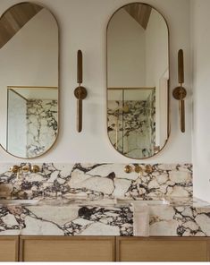 two mirrors are hanging on the wall above a marble counter top with gold accents and brass faucets