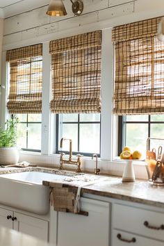 a kitchen with white cabinets and windows covered in roman shades that are hung above the sink