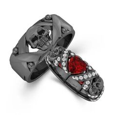 two wedding bands with skulls on them and red stones in the middle, set against a white background