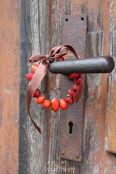 a door handle with a red beaded wreath hanging on it's side next to a wooden door