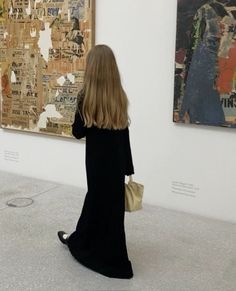 a woman is looking at art on display in a museum with paintings hanging behind her