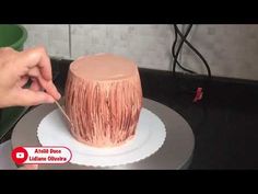 a person is decorating a cake with pink icing on a plate and holding a stick