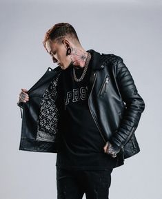 a man with tattoos and piercings wearing a black leather jacket standing in front of a white background