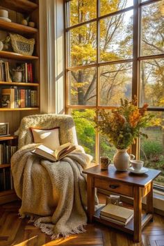 A cozy reading nook with a plush armchair by a large window, letting in warm, golden sunlight. A soft blanket is draped over the arm of the chair, and a steaming cup of tea rests on a small wooden table nearby. The shelves are stacked with books, some open, some piled high. In the background, there’s a leafy plant adding a touch of nature. The setting exudes a peaceful, inviting atmosphere, perfect for diving into a good book. Cozy Fall Reading Nook, Cozy Home Style, Cozy Book Nook Aesthetic, Cozy Nook Ideas Reading Areas, Reading Chair Aesthetic, Cozy Home Vibes, Upstairs Sunroom, Cosy Living Room Ideas Warm Colours, Cozy Reading Space