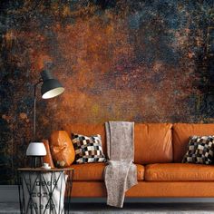 an orange leather couch sitting in front of a wall covered in rust and black paint