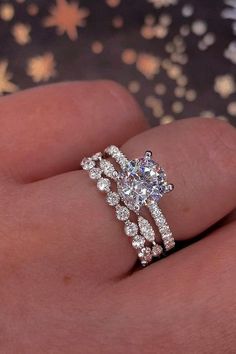 a woman's hand with a diamond ring on top of her finger and the other hand holding an engagement ring