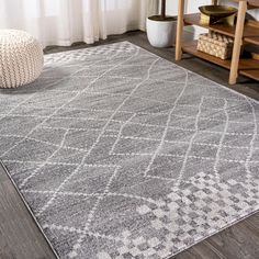 a gray rug with white and grey designs on the floor in front of a window