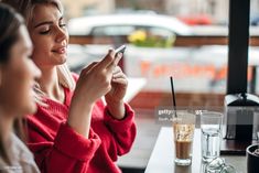 two women are sitting at a table looking at their cell phones while one looks at her phone