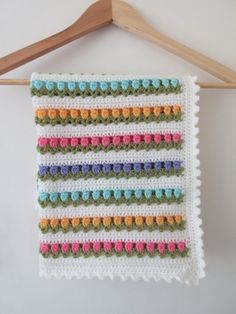 a multicolored crocheted blanket hanging from a wooden hanger on a white wall