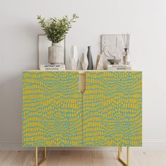 a yellow and blue cabinet sitting on top of a hard wood floor next to a potted plant