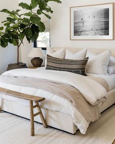 a bed with white sheets and pillows next to a potted plant in a bedroom