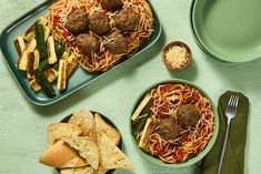 two plates of spaghetti, meatballs and veggies on a green tablecloth