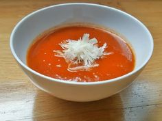 a white bowl filled with tomato soup on top of a wooden table and topped with shredded cheese