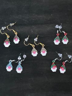 six pairs of earrings are displayed on a black surface with white, pink and blue beads