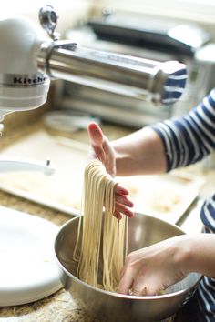 a woman is holding noodles in a bowl on the kitchen counter top while using a hand mixer