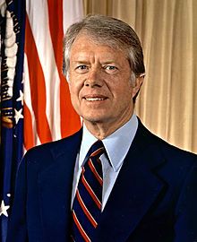 a man wearing a suit and tie standing in front of american flags