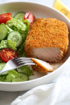 a white bowl filled with meat, salad and cucumbers next to a fork